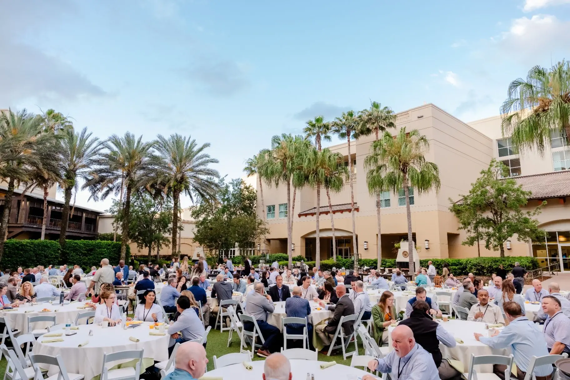 Guests seated for an outdoor corporate luncheon at a palm-lined venue
